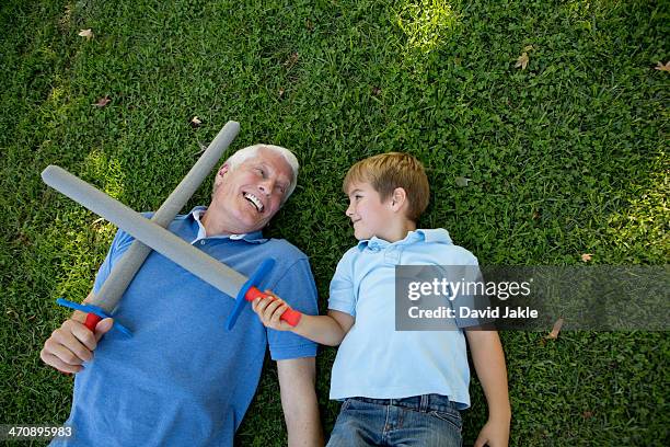 grandfather and grandson lying on grass with toy swords - toy sword stock pictures, royalty-free photos & images