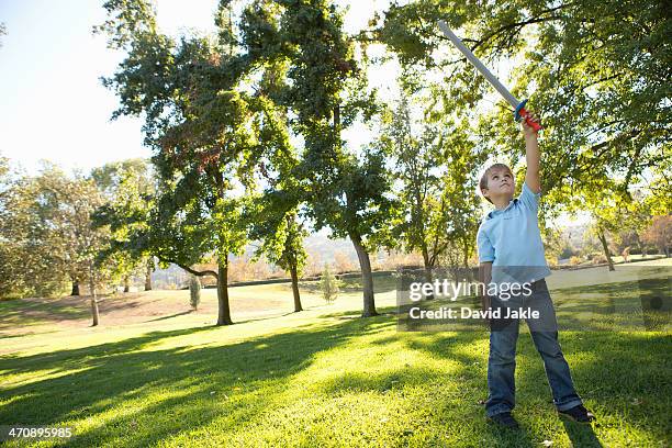 boy in park raising toy sword in air - toy sword stock pictures, royalty-free photos & images