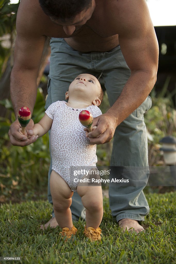Grandfather helping granddaughter to walk holding rattles