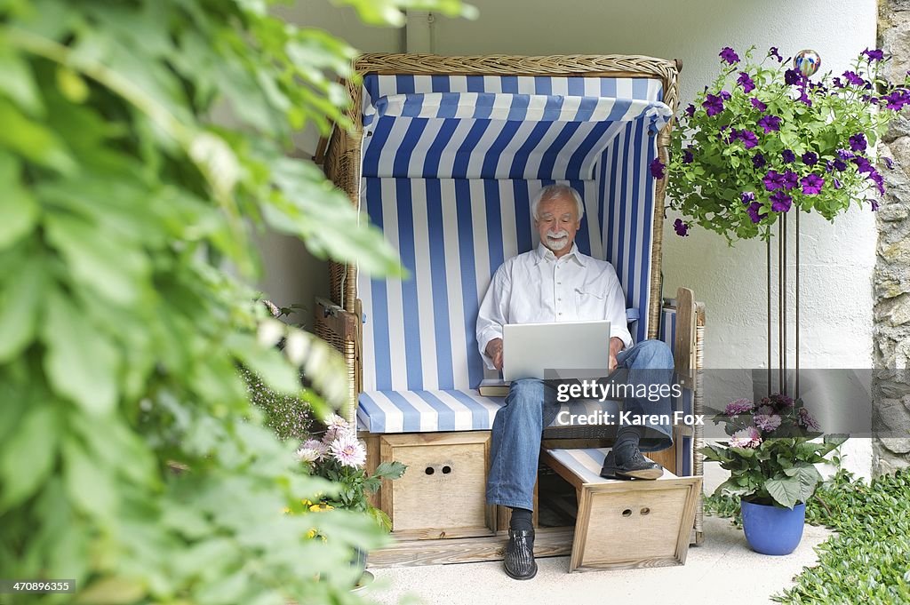 Senior man using laptop on garden seat