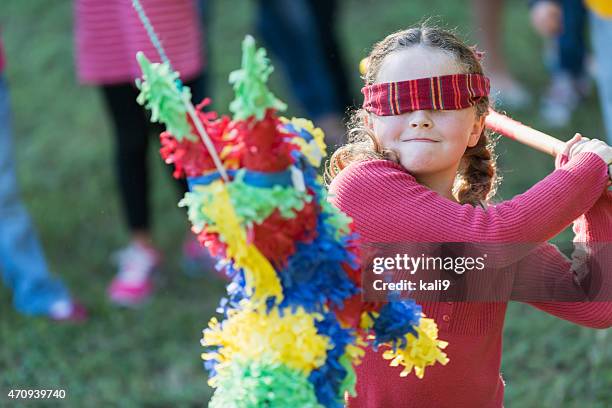 little girl wearing venda de ojos pulsando una piñata - pinata fotografías e imágenes de stock