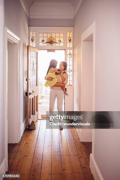 mother carrying her daughter into the hall of their home - front door open stock pictures, royalty-free photos & images