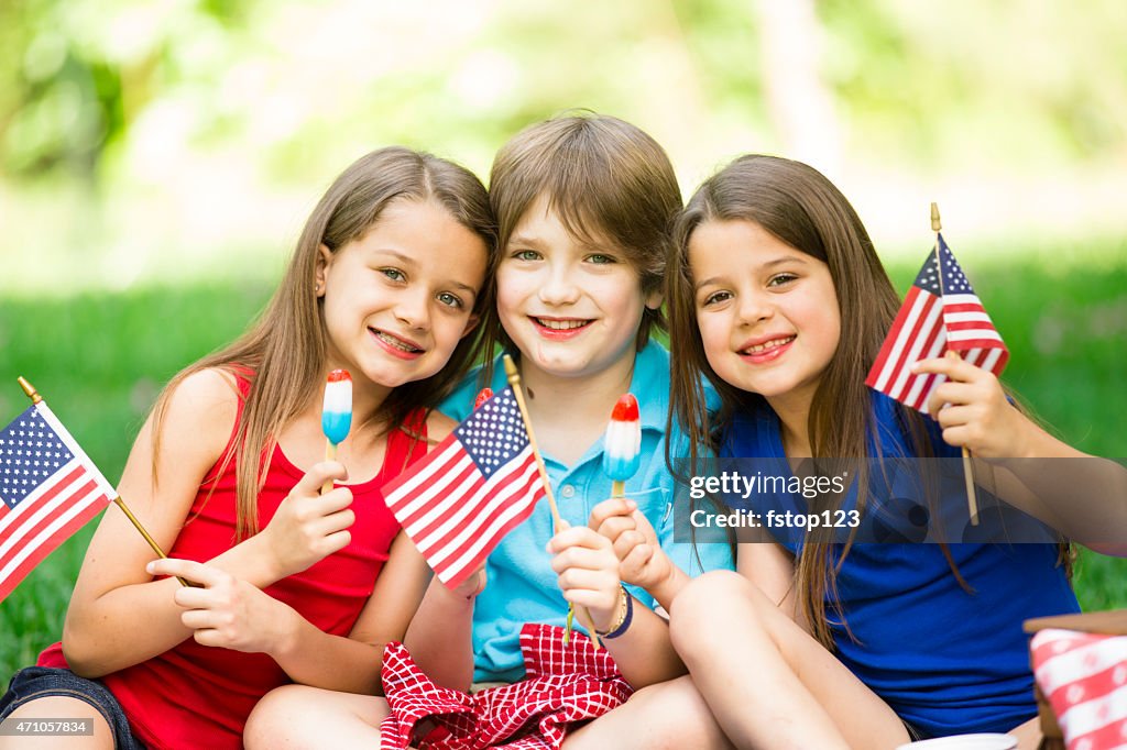 Children enjoy July 4th picnic in summer. American flags, popsicles.