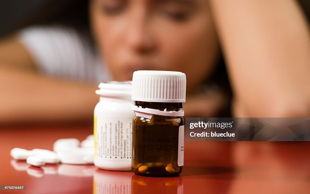 Pill bottles with pills next to them and a woman in back