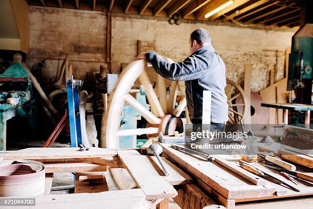 skilled wheelwright, in his workshop, rolls a wooden cartwheel - colyton stockfoto's en -beelden