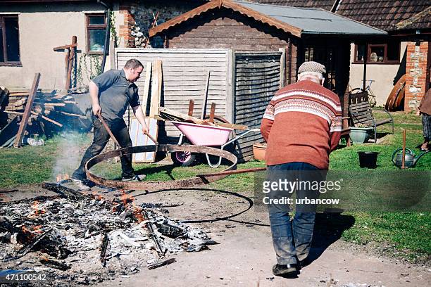 traditional wheelwrights lifting the metal tyre for a wooden cartwheel - colyton stock pictures, royalty-free photos & images