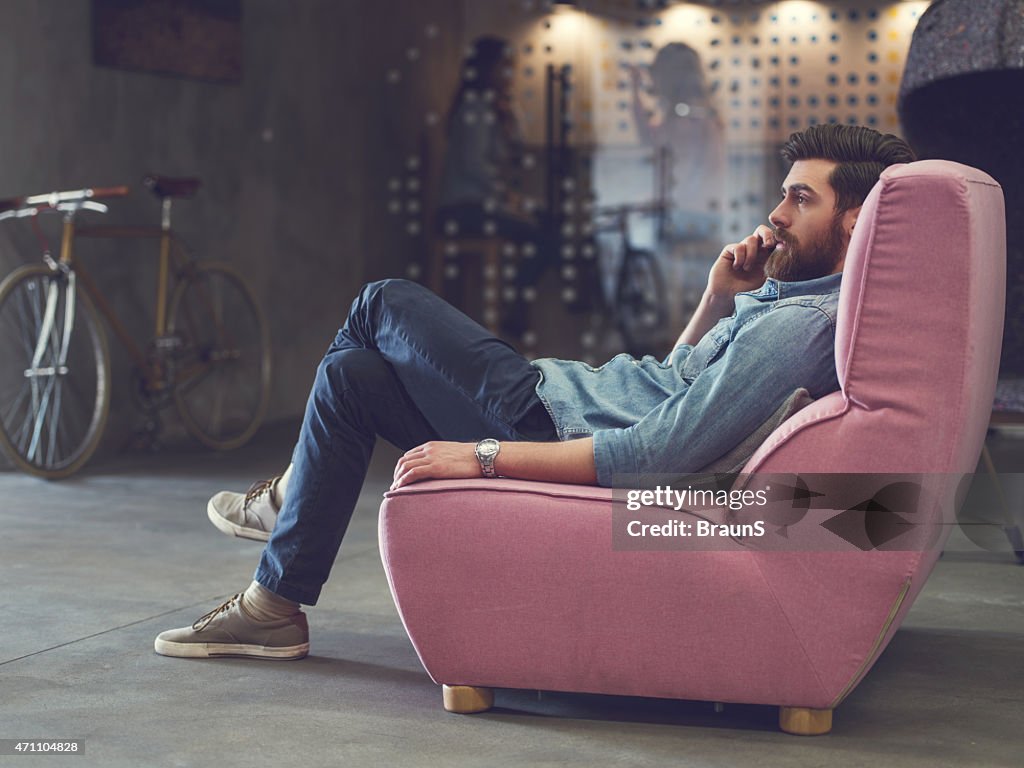 Young man relaxing in armchair and talking on the phone.