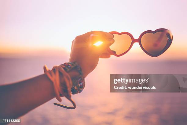 hand hält herz-sonnenbrille am strand bei sonnenuntergang - girl beach sunset stock-fotos und bilder