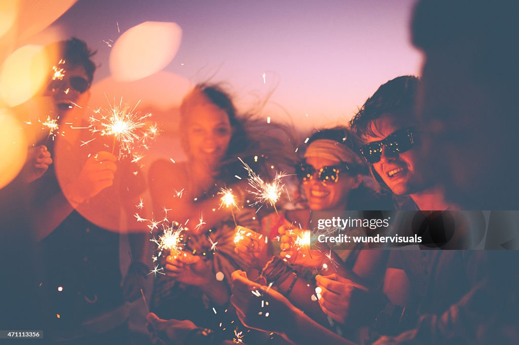 Friends holding sparklers at a beachparty at twilight