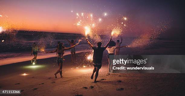 freunde laufen mit feuerwerk am strand nach dem sonnenuntergang - strand stock-fotos und bilder