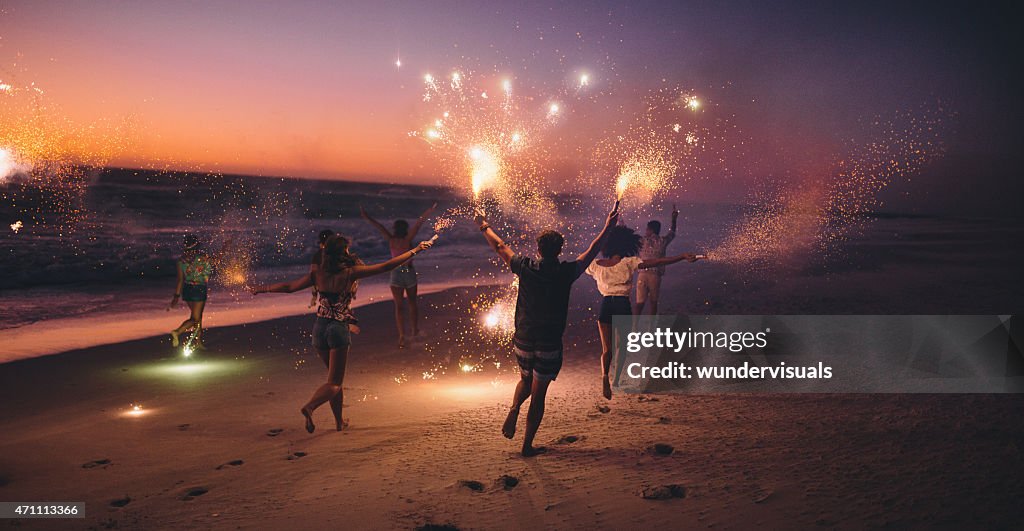 Amigos corriendo con fuegos artificiales en la playa después de la puesta de sol