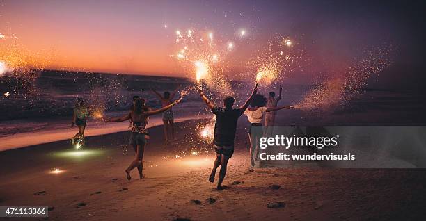 amis courir avec feux d'artifice sur la plage après le coucher du soleil - summer party photos et images de collection