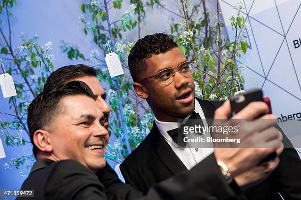 Russell Wilson, player for Seattle Seahawks, right, poses for a "selfie" photograph with guests as he attends the Bloomberg cocktail party before the...
