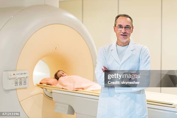 sonriendo médico s'encuentra junto a un escáner de mri. - pet scan machine fotografías e imágenes de stock