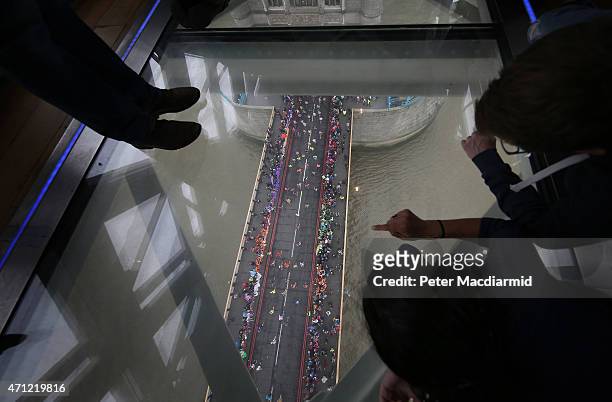 Visitors to Tower Bridge's Exhibition glass walkway watch runners on The Virgin Money London Marathon cross the River Thames on April 26, 2015 in...