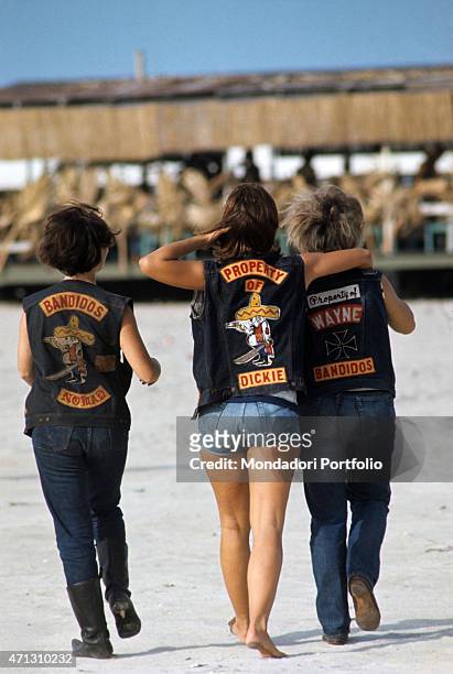 Three girls from the Bandidos gang, shot from behind walking on the beach, wearing their biker jackets. Texas , September 1969.
