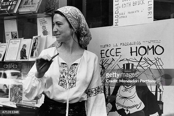 The writer Barbara Alberti wears a scarf and smokes a long cigarette close to the poster of her theatre work Ecce Homo. Rome , 1974.