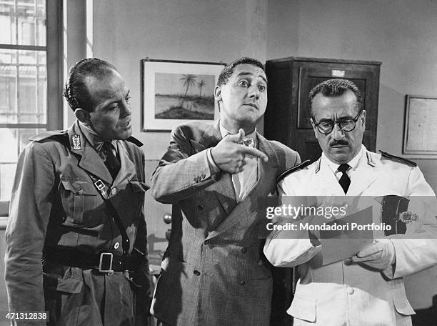 Italian actor Peppino De Filippo, dressed as a traffic policeman, reading a paper beside Italian actor Alberto Sordi in the film Piccola posta. 1955