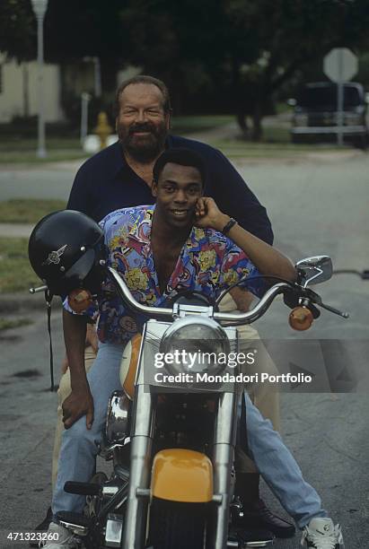 Italian actor Bud Spencer and American actor Michael Winslow posing on a motorbike on the set of the TV series Extralarge. 1992