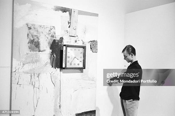 Boy comparing the time on his watch to the time shown by the combine painting Third Time Painting by Robert Rauschenberg at the 32nd Art Biennale. On...