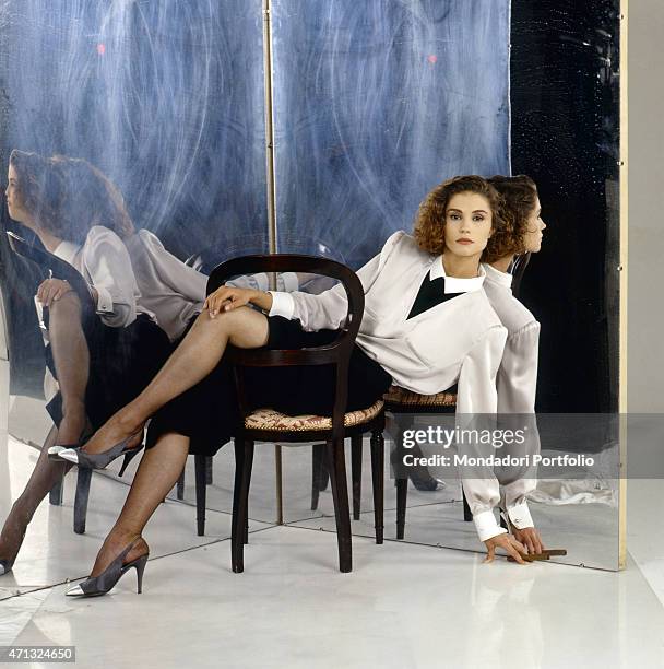 Italian-born French showgirl Alessandra Martines posing seated on a chair. 1989