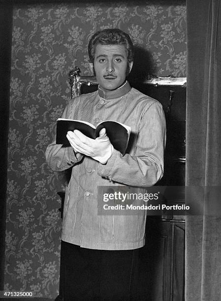 Italian singer-songwriter and actor Domenico Modugno in porter's uniform holding a book. 1950s