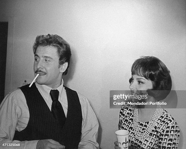 Italian singer-songwriter and actor Domenico Modugno smoking a cigarette beside Italian actress Gina Lollobrigida. 1960s