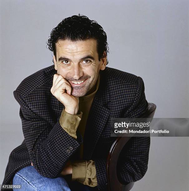 Italian actor and director Massimo Troisi smiling sitting on a chair. 1989