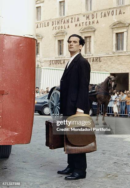 Italian actor and director Massimo Troisi posing holding some suitcases in front of the nursery school Margherita di Savoia in the film Le vie del...