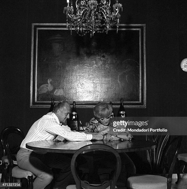 Italian TV artists Raimondo Vianello and Sandra Mondaini sitting at the table and caressing their cat. 1967