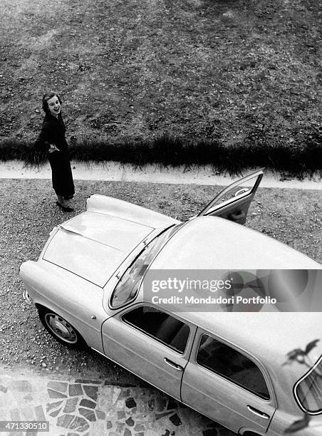 Italian actress Anna Maria Ferrero smiling beside an Alfa Romeo Giulietta. Milan, April 1955