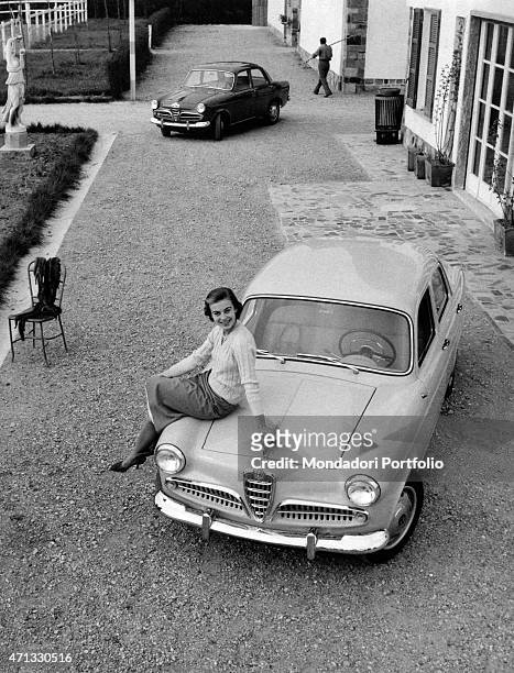 Italian actress Anna Maria Ferrero sitting on the car bonnet of an Alfa Romeo Giulietta. Milan, April 1955