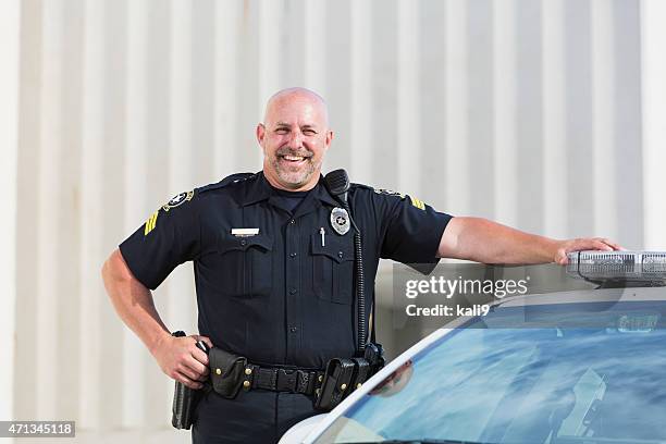 happy police officer standing next to cruiser - police uniform stockfoto's en -beelden