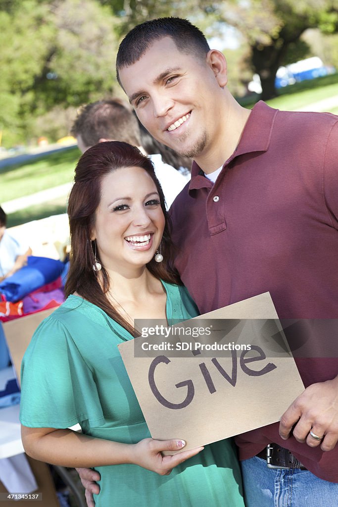 Couple holding ""Give"" sign at donations center
