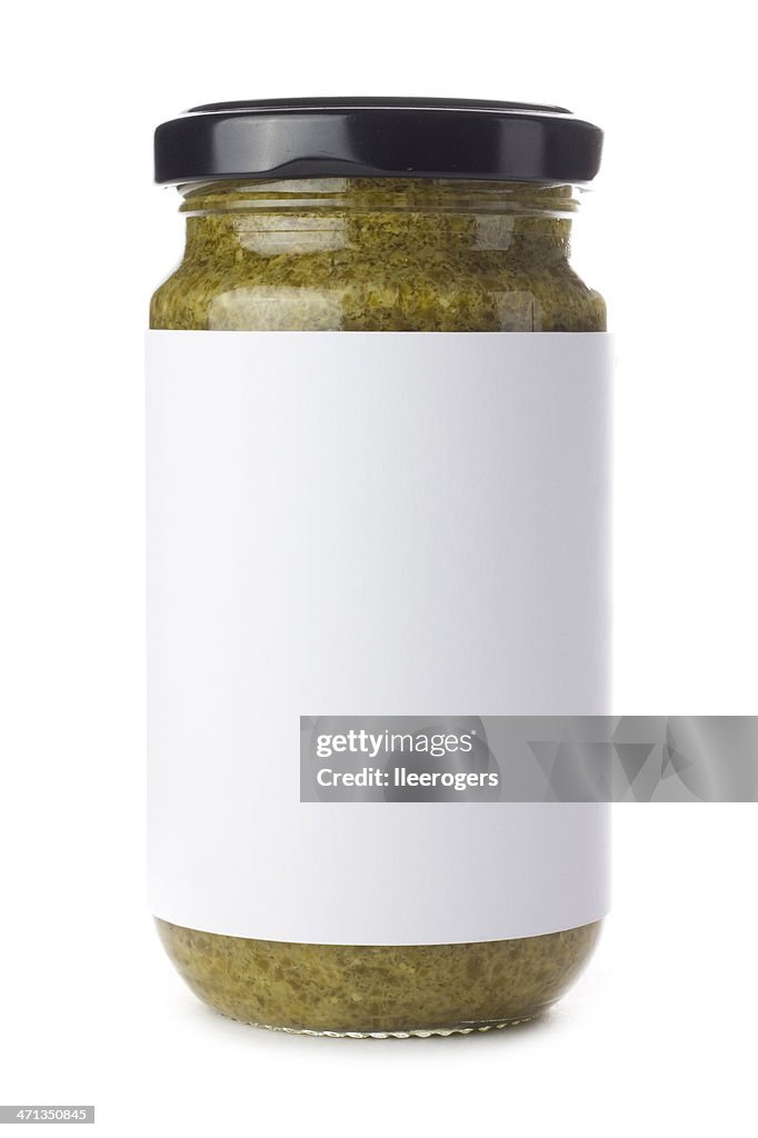 Glass jar of green pesto on a white background