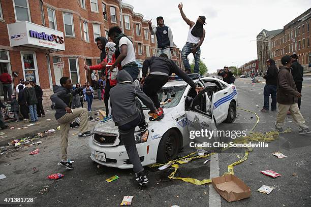 Demonstrators climb on a destroyed Baltimore Police car in the street near the corner of Pennsylvania and North avenues during violent protests...