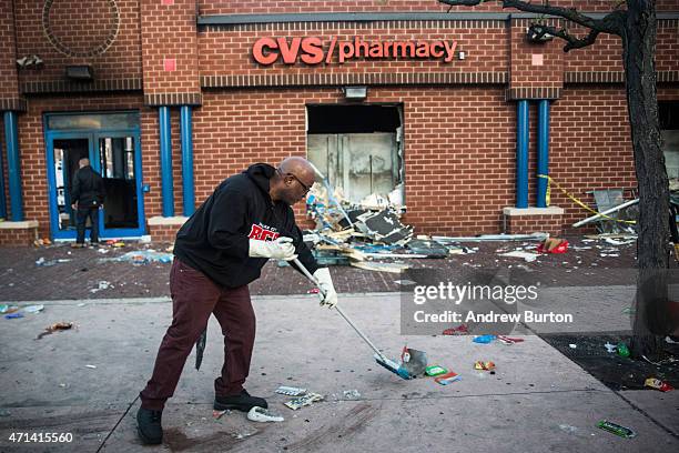 Jerald Miller helps clean up debris from a CVS pharmacy that was set on fire yesterday during rioting after the funeral of Freddie Gray, on April 28,...