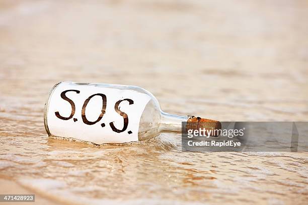 sos message in bottle being washed away by tide - sos stock pictures, royalty-free photos & images