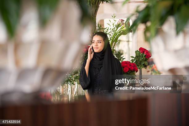 traditionally dressed middle eastern woman with flowers talking on cellphone - arab shopping stock pictures, royalty-free photos & images