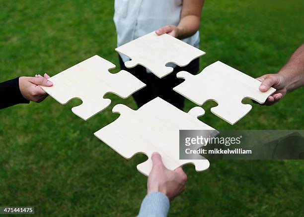 four different people connecting large puzzle pieces - four people stockfoto's en -beelden