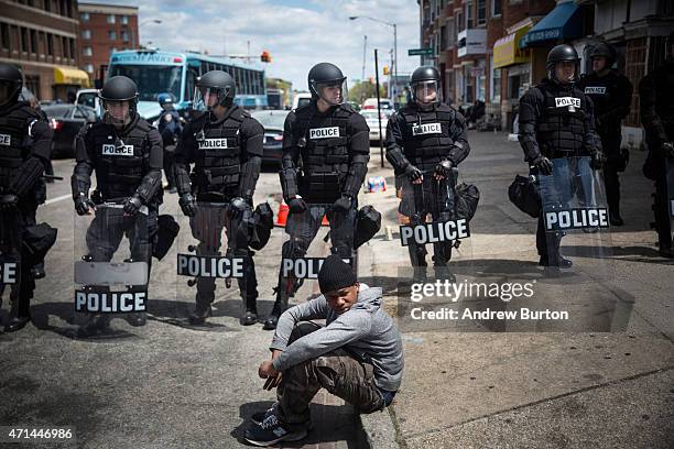 Daquan Green, age 17, sits on the curb while riot police stand guard near the CVS pharmacy that was set on fire yesterday during rioting after the...