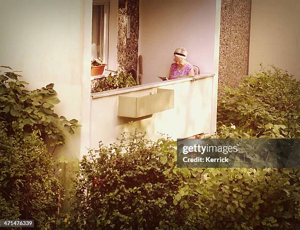 senior frau liest ein buch auf dem balkon - plattenbau stock-fotos und bilder