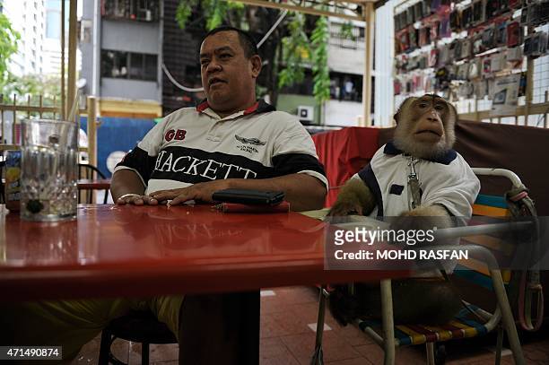 This photo taken on April 25, 2015 shows Jamil Ismail talking to a friend as his male monkey named "JK" looks on after their lunch at a restaurant in...