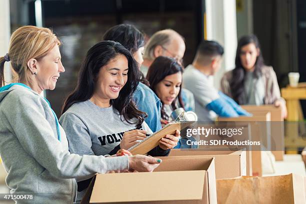 diverse adults packing donation boxes in charity food bank - schenking stockfoto's en -beelden
