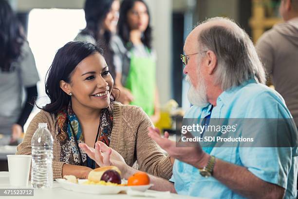 young woman volunteering in food bank and talking to senior - soup kitchen stock pictures, royalty-free photos & images