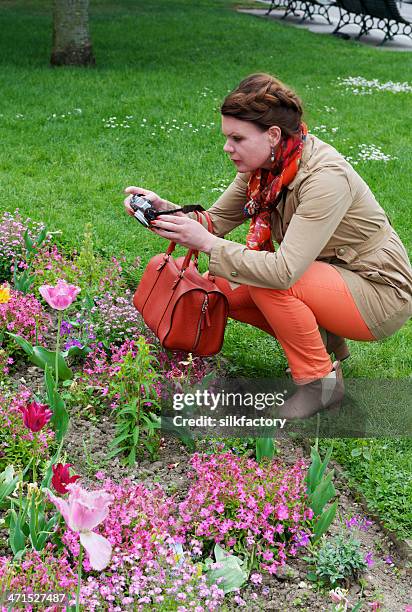 elegante mujer tomando fotografías de flores de primavera en el parque de parís - bolso naranja fotografías e imágenes de stock