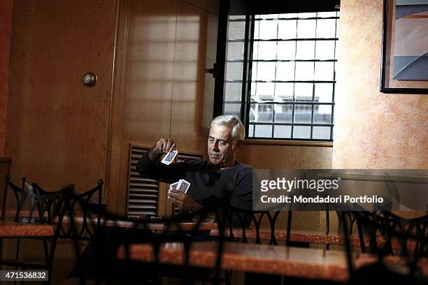 "The famous comic actor and anchorman Teo Teocoli, seated at a table of the coffee bar Vega, plays cards by himself; he started as a cabaret artist...
