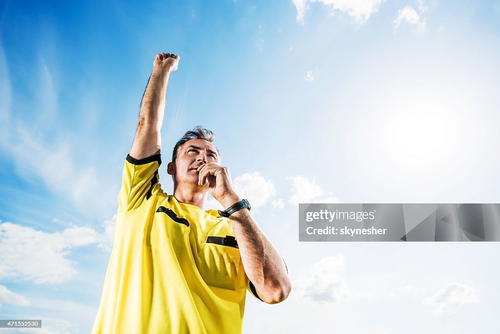 Soccer referee blowing his whistle against the sky.