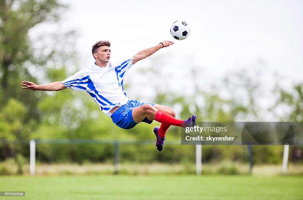 Soccer player kicking the ball while being in mid air.