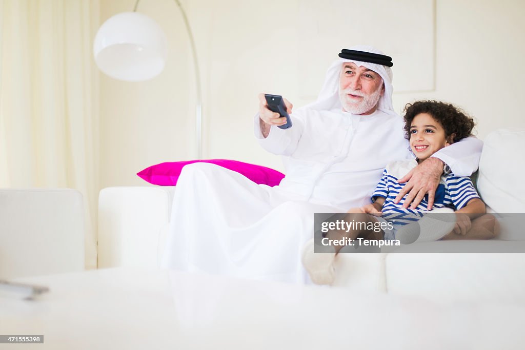 Middle eastern grandfather watching tv at home with grandson.